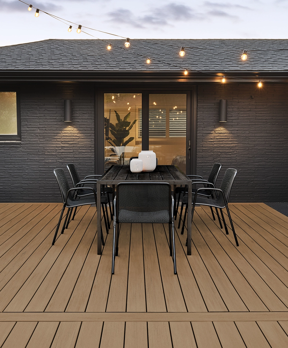 Light TimberTech Coconut Husk PVC deck with black-framed sliding doors, modern dining table, and string lights on a contemporary home.