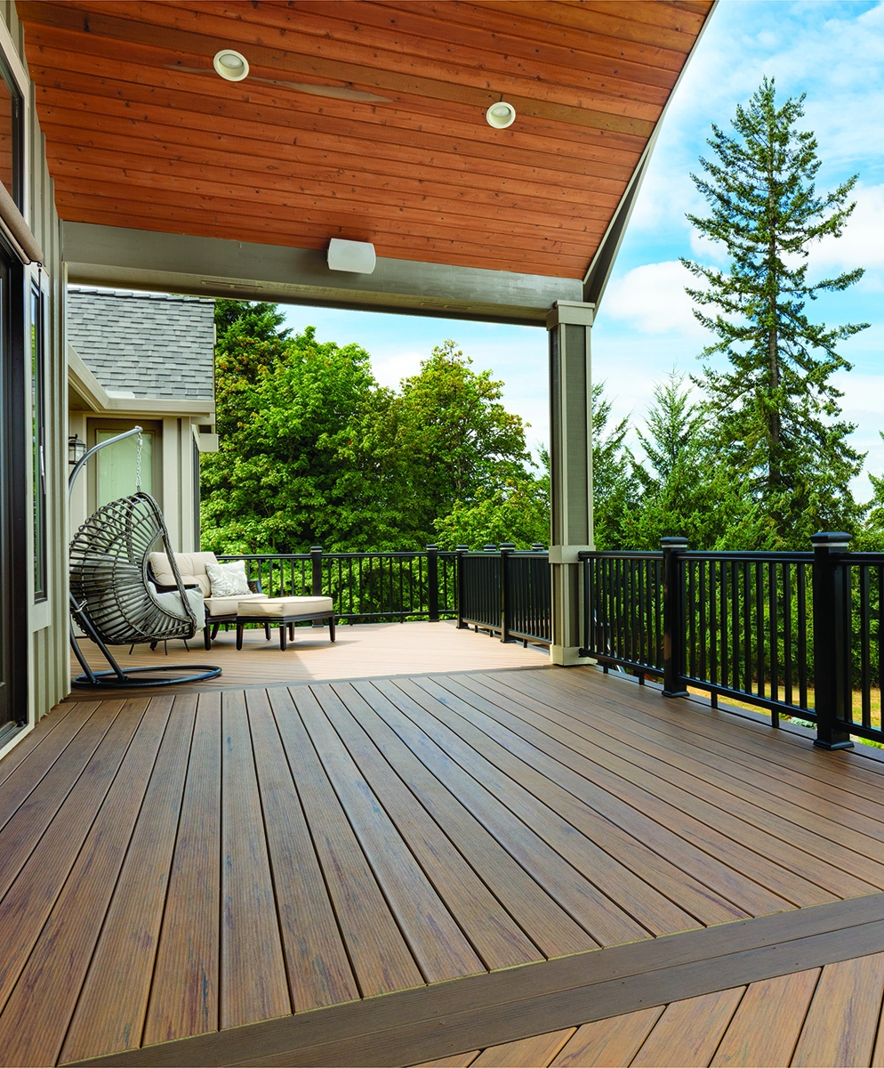 TimberTech Tigerwood and Mocha composite deck with dark railing and conversation seating surrounded by tall trees.